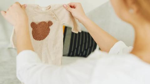 Žena drží malé body s medvídkem při přípravě věcí do porodnice