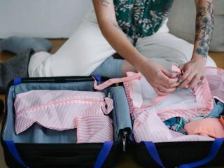 Žena balí oblečení do otevřeného kufru · Foto: Timur Weber / Pexels Žena balí pruhované oblečení do otevřeného kufru, ilustrace balení tašky do porodnice